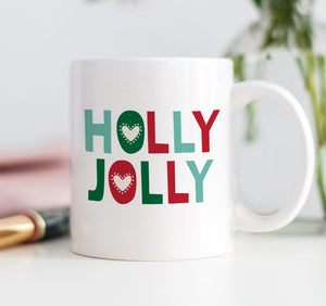 A white ceramic coffee mug with the vibrant, bold words HOLLY JOLLY printed in hues of red and green in a modern, trendy, fun, and festive font.