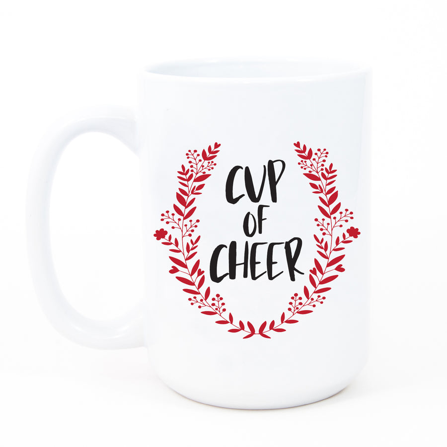 Cup of Cheer Coffee Mug with bold black festive text and a red wreath Christmas emblem on a fine white ceramic mug.