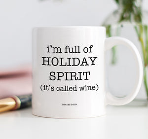 A white ceramic coffee mug with I'm Full of Holiday Spirit It's Called Wine printed in playful, modern font.